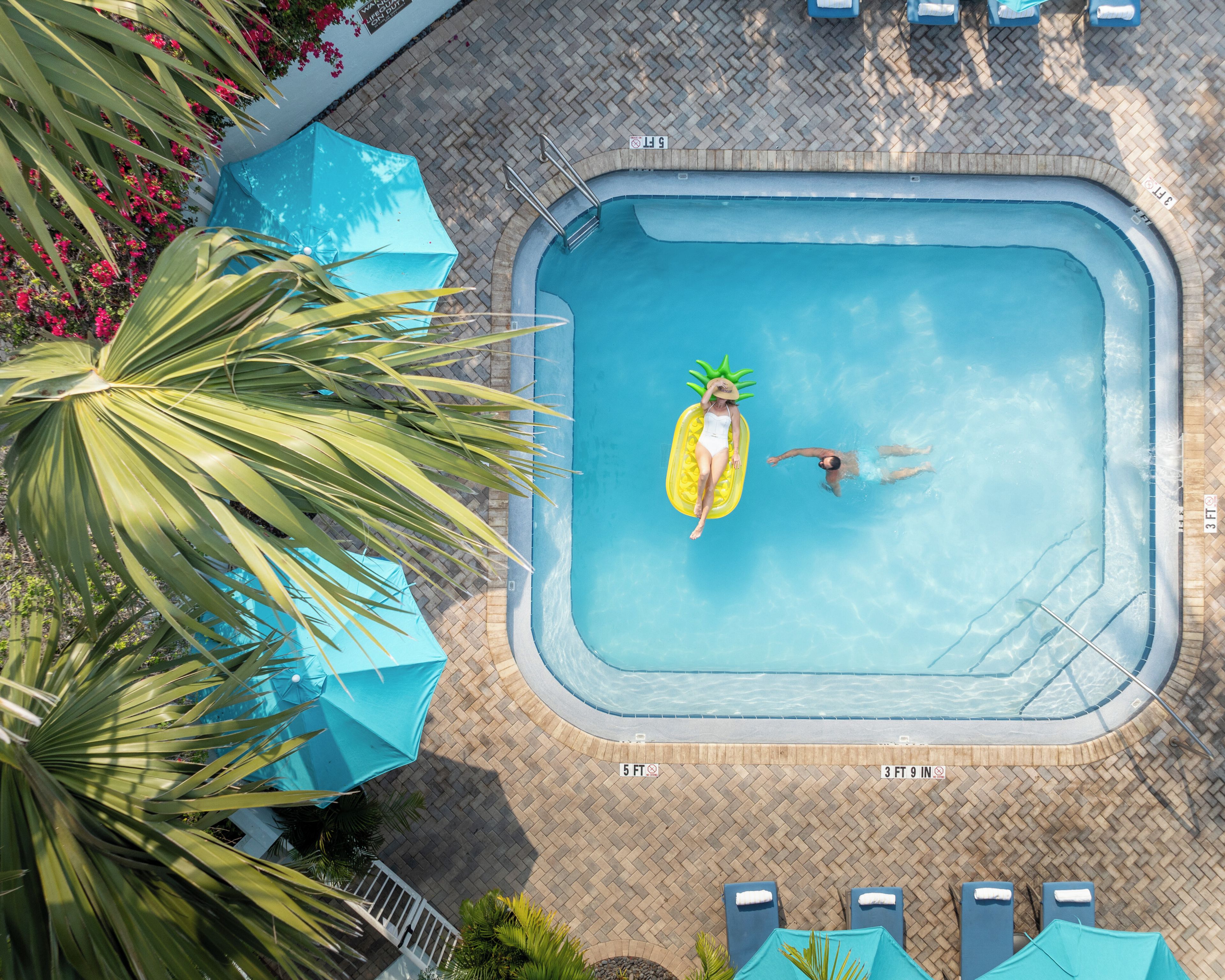 An aerial view of a swimming pool with a lifeguard, lounge chairs, and umbrellas.