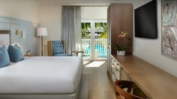 A hotel room with a large bed, a desk, a chair, a TV, and a view of a pool.