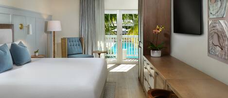 A hotel room with a large bed, a desk, a chair, a TV, and a view of a pool.