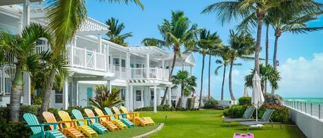 A beachfront hotel with colorful Adirondack chairs, a pool area, and a view of the ocean.