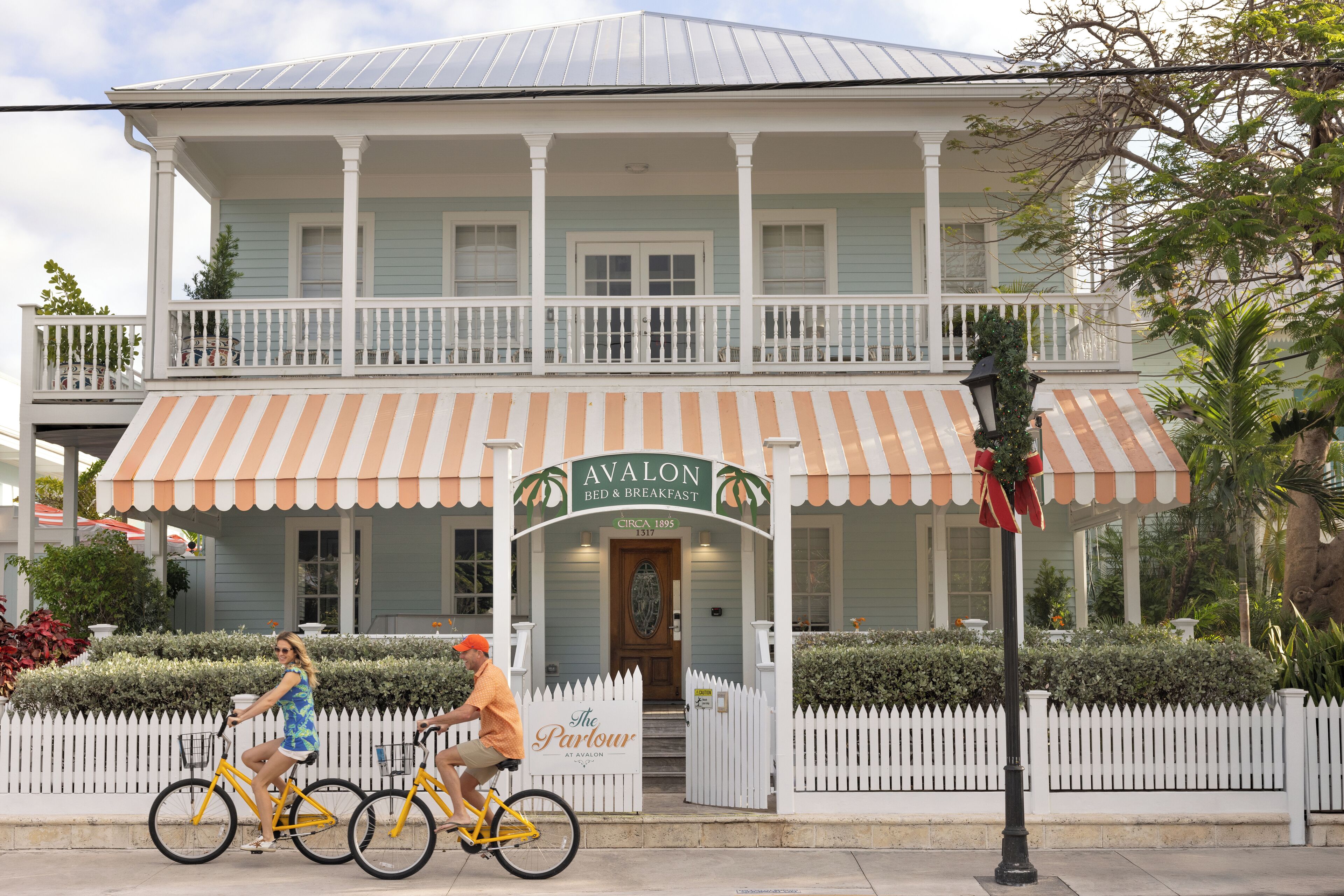 A two-story building with a porch, a sign reading "Avalon Bed & Breakfast," and a white picket fence.