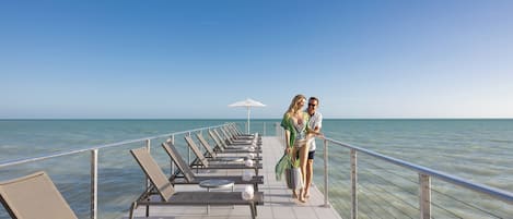 Une terrasse dotée de chaises longues et d’une rambarde offrant une vue sur la mer.