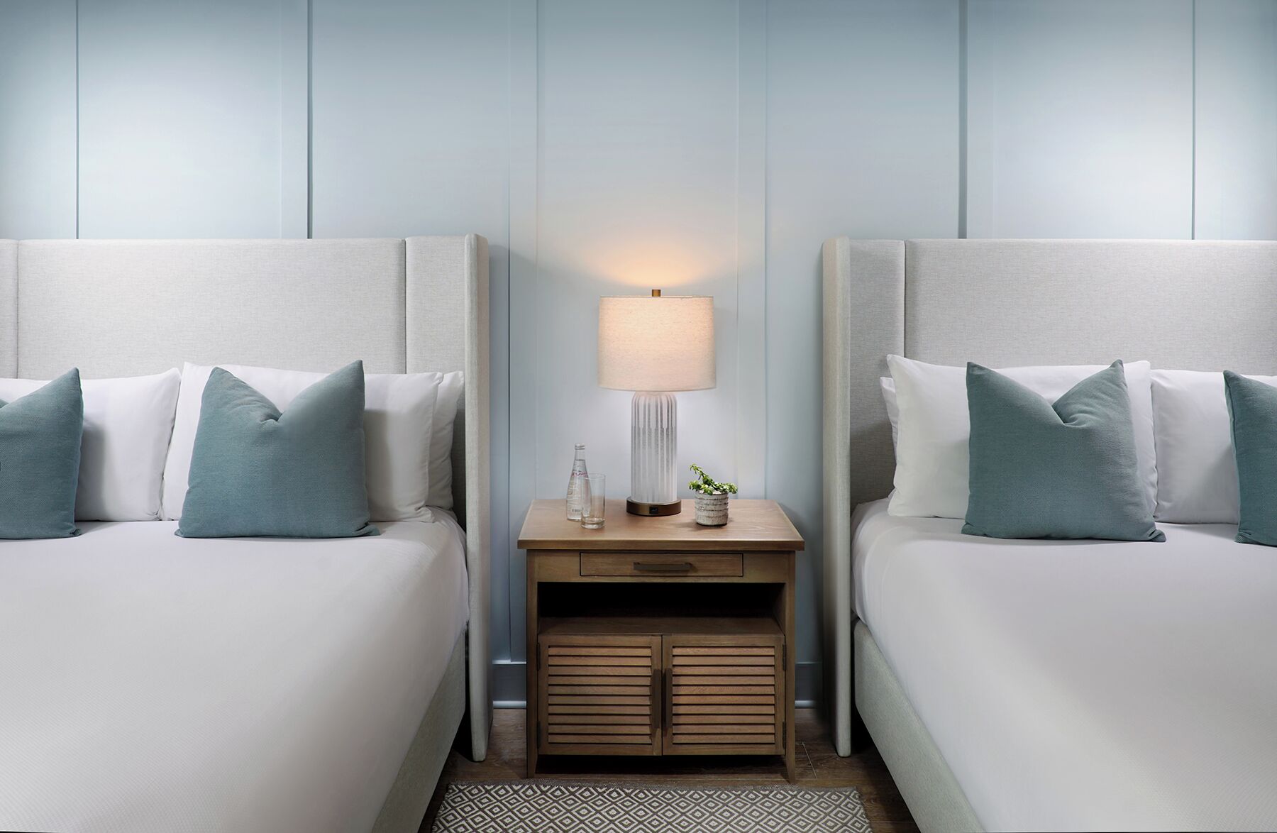 A hotel room with two beds, a nightstand with a lamp, and a small cabinet.