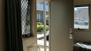 A small room with a table and chairs, a window with curtains, and a door leading outside. - Travellers Motor Village (Mayfield West)