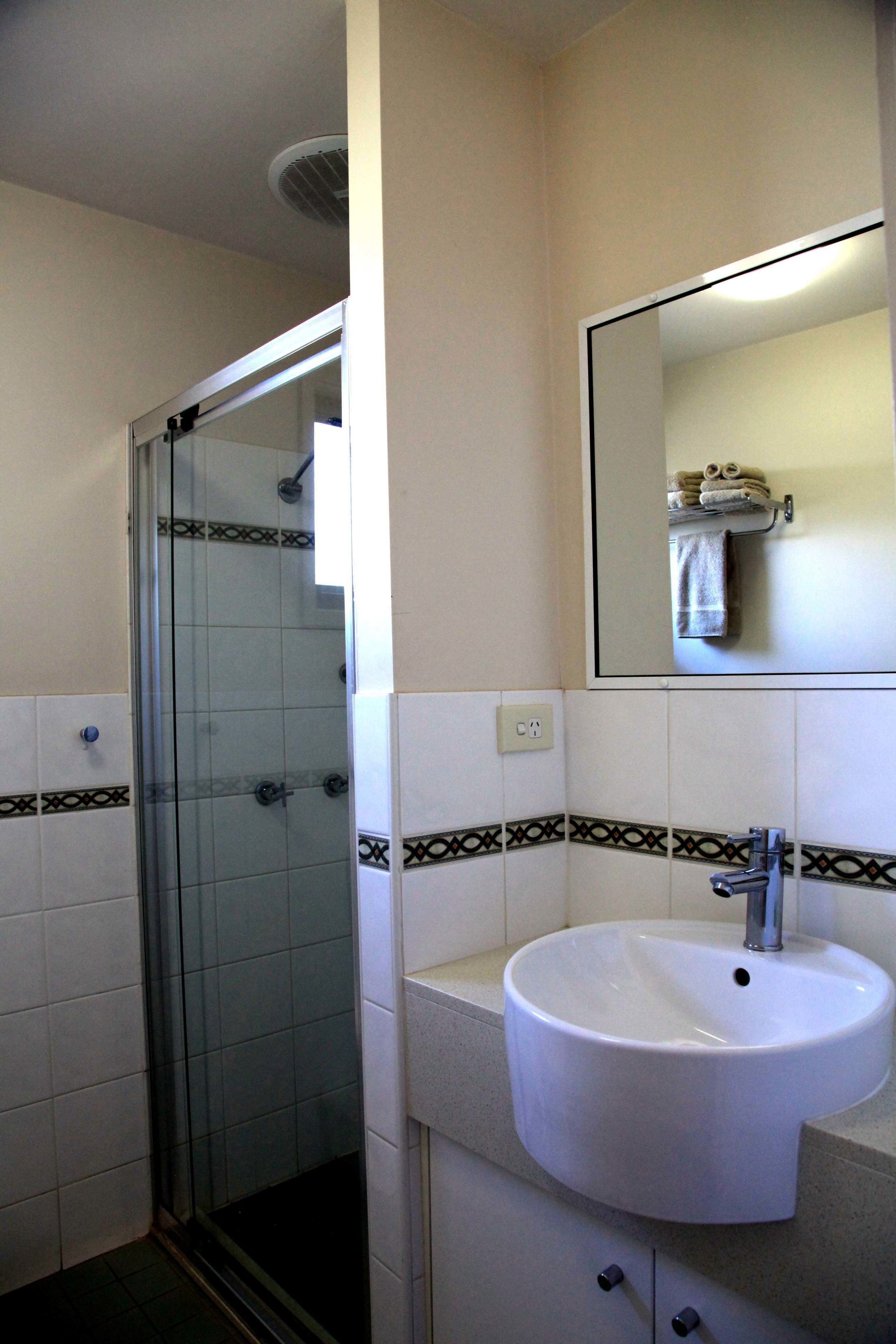 Une salle de bain avec une douche à parois de verre, un lavabo blanc et un miroir au-dessus.