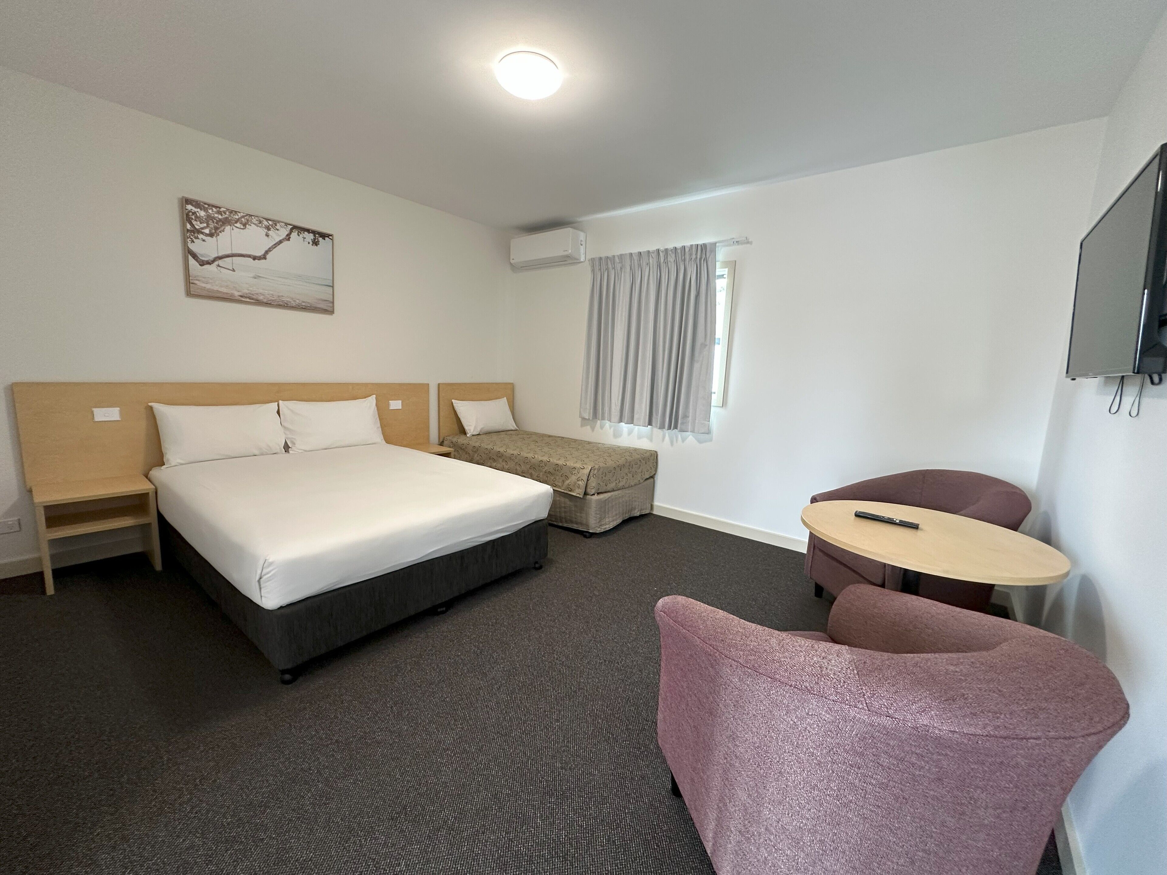 Habitación de hotel con una cama grande, una cama más pequeña, un escritorio, una silla y un televisor.