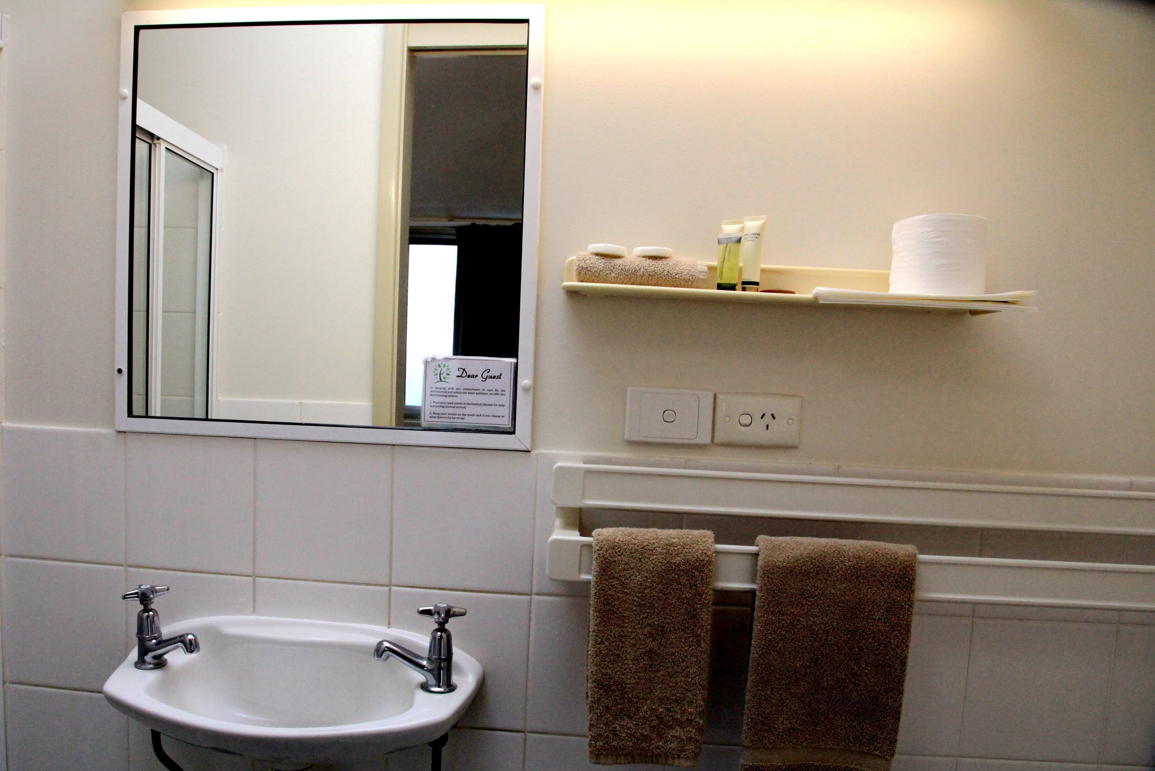A bathroom with a sink, mirror, towel rack, and toiletries shelf.