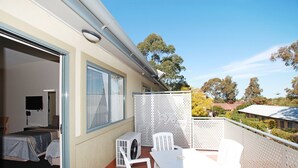 A balcony with a table and chairs, a white partition, and a view of trees and houses. - Travellers Motor Village (Mayfield West)