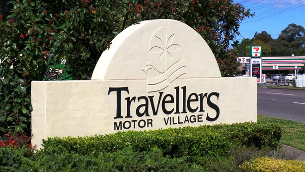 A sign for Travellers Motor Village with a logo of a car and a bird. - Travellers Motor Village (Mayfield West)