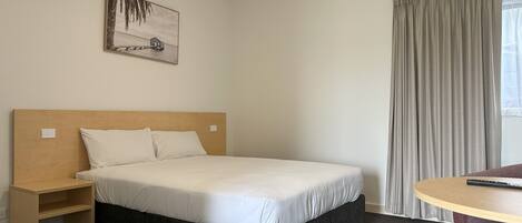Una habitación de hotel con una cama individual, una mesita de noche de madera, una pequeña mesa y una silla.