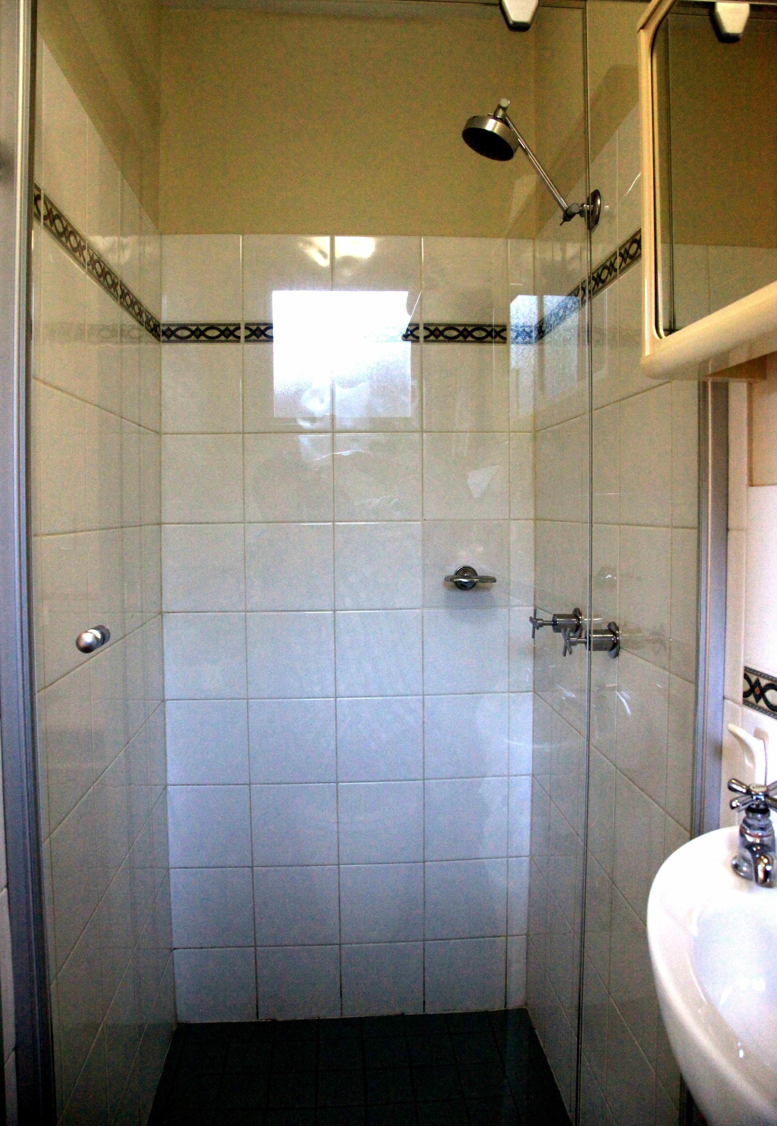 A shower with a glass door, a handheld showerhead, and a wall-mounted faucet.