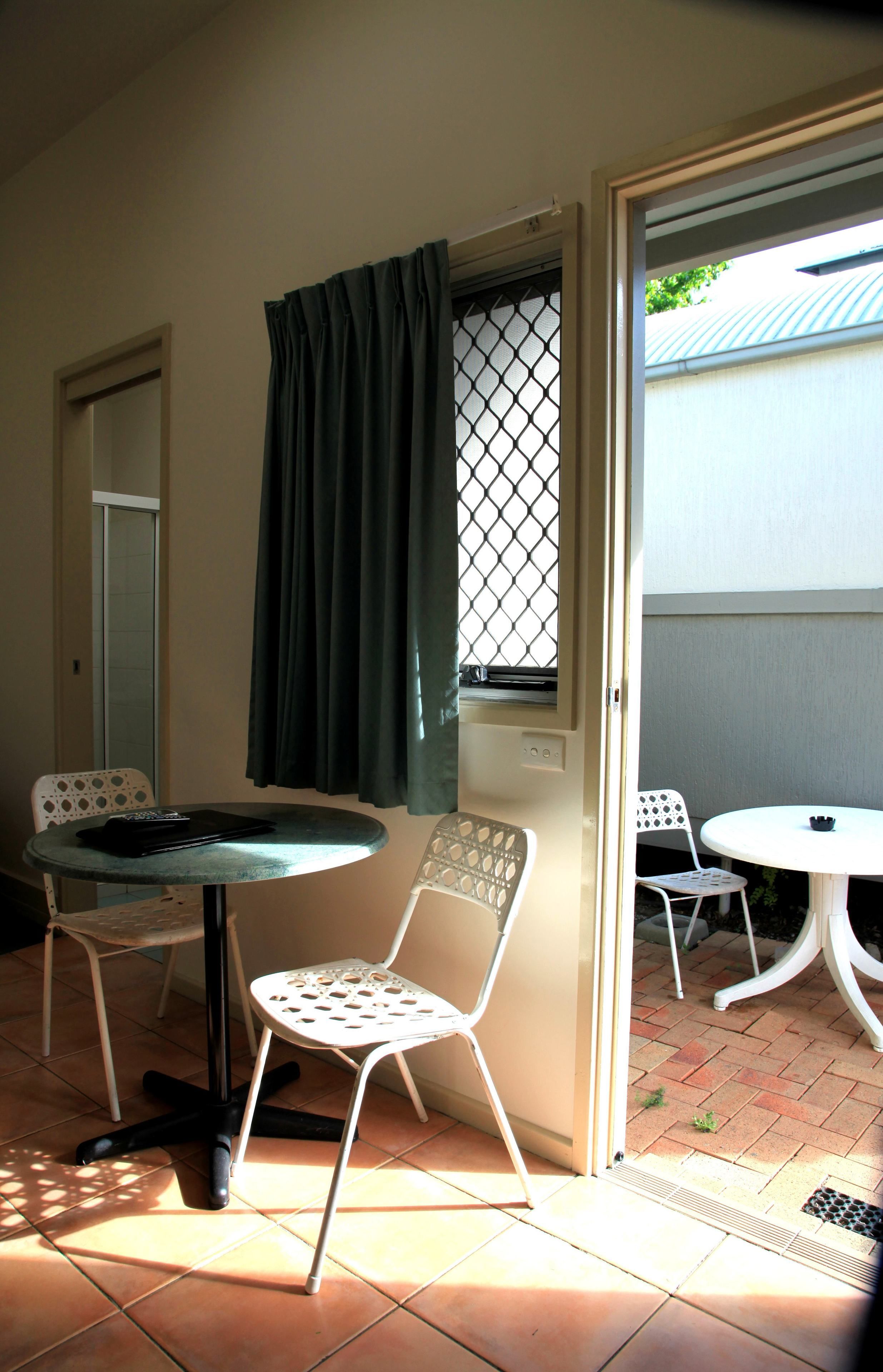 A room with two white chairs, a small round table, a window with a metal screen, and a door.