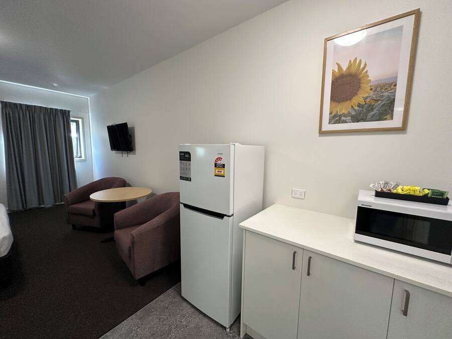 Habitación de hotel compacta con kitchenette, zona de comedor con una mesa y dos sillas, refrigerador, microondas y televisor montado en la pared.