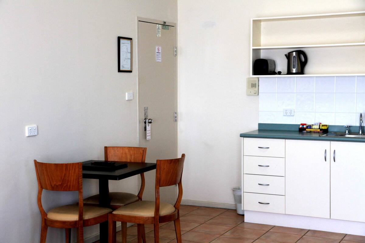 A small kitchen with a dining table and chairs, a white cabinet with a sink, and a tiled backsplash.