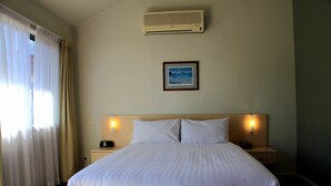 A hotel room with a large bed, two bedside tables with lamps, a wall-mounted air conditioner, and a framed picture above the bed. - Travellers Motor Village (Mayfield West)
