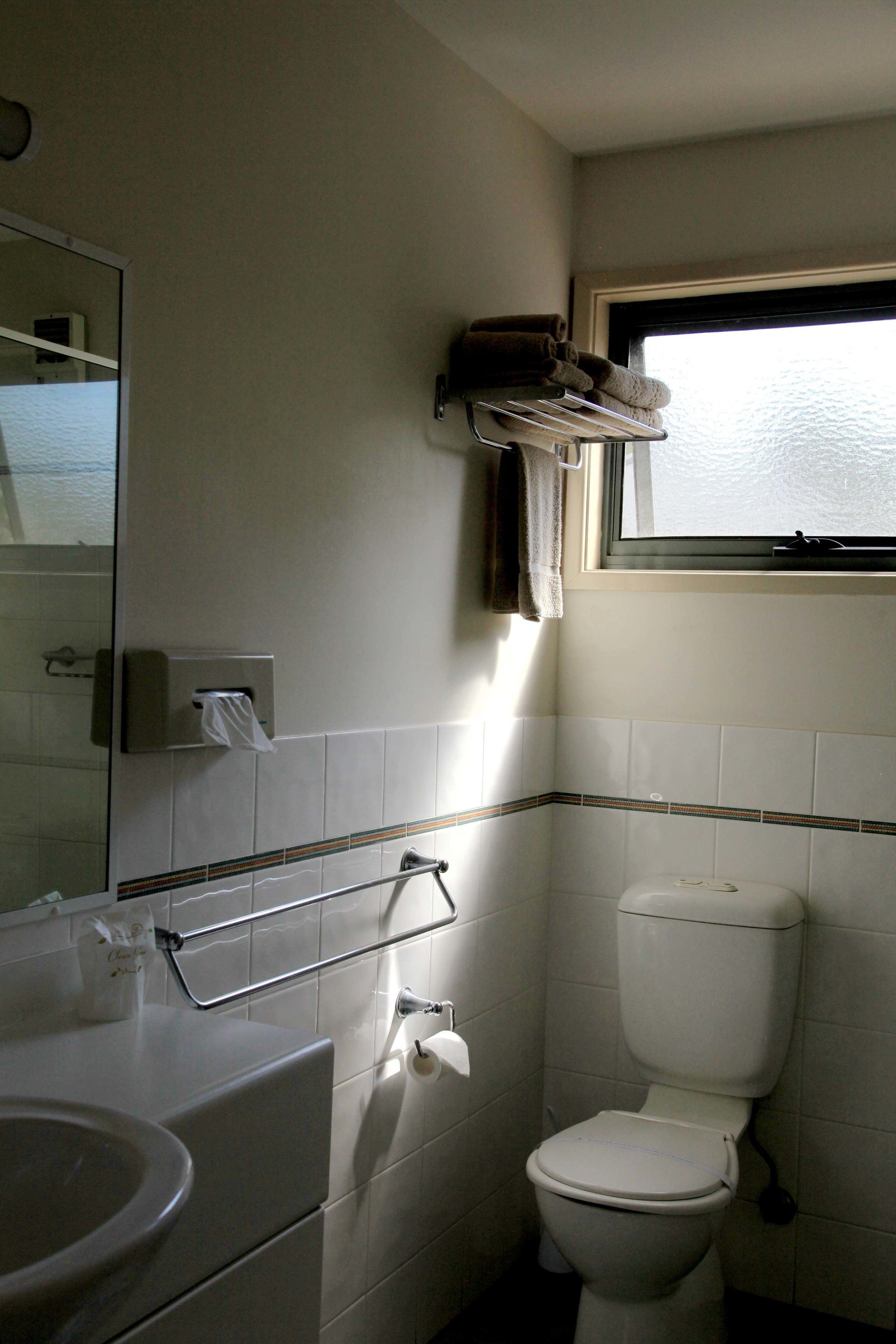 Une petite salle de bain comprenant des toilettes, un lavabo, un porte-serviettes et une fenêtre.