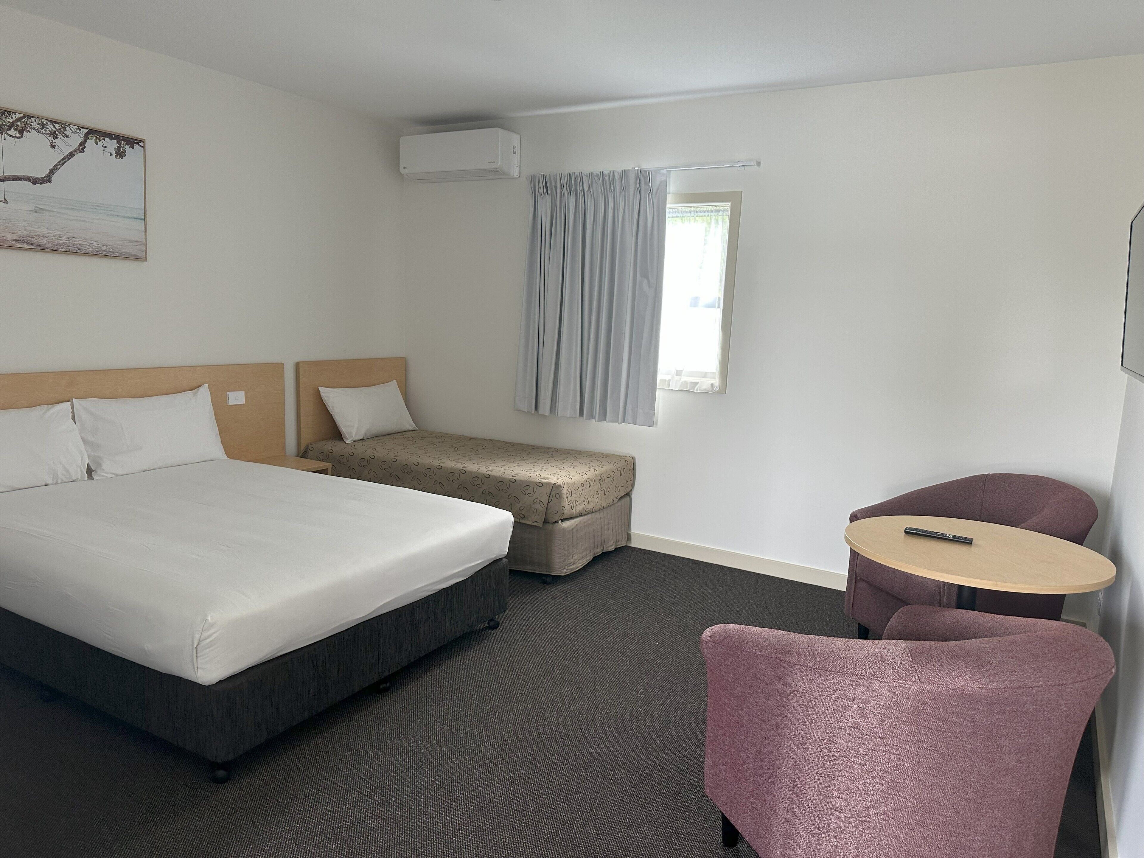 Una habitación de hotel con una cama grande, una cama más pequeña, un escritorio, una silla y un equipo de aire acondicionado.