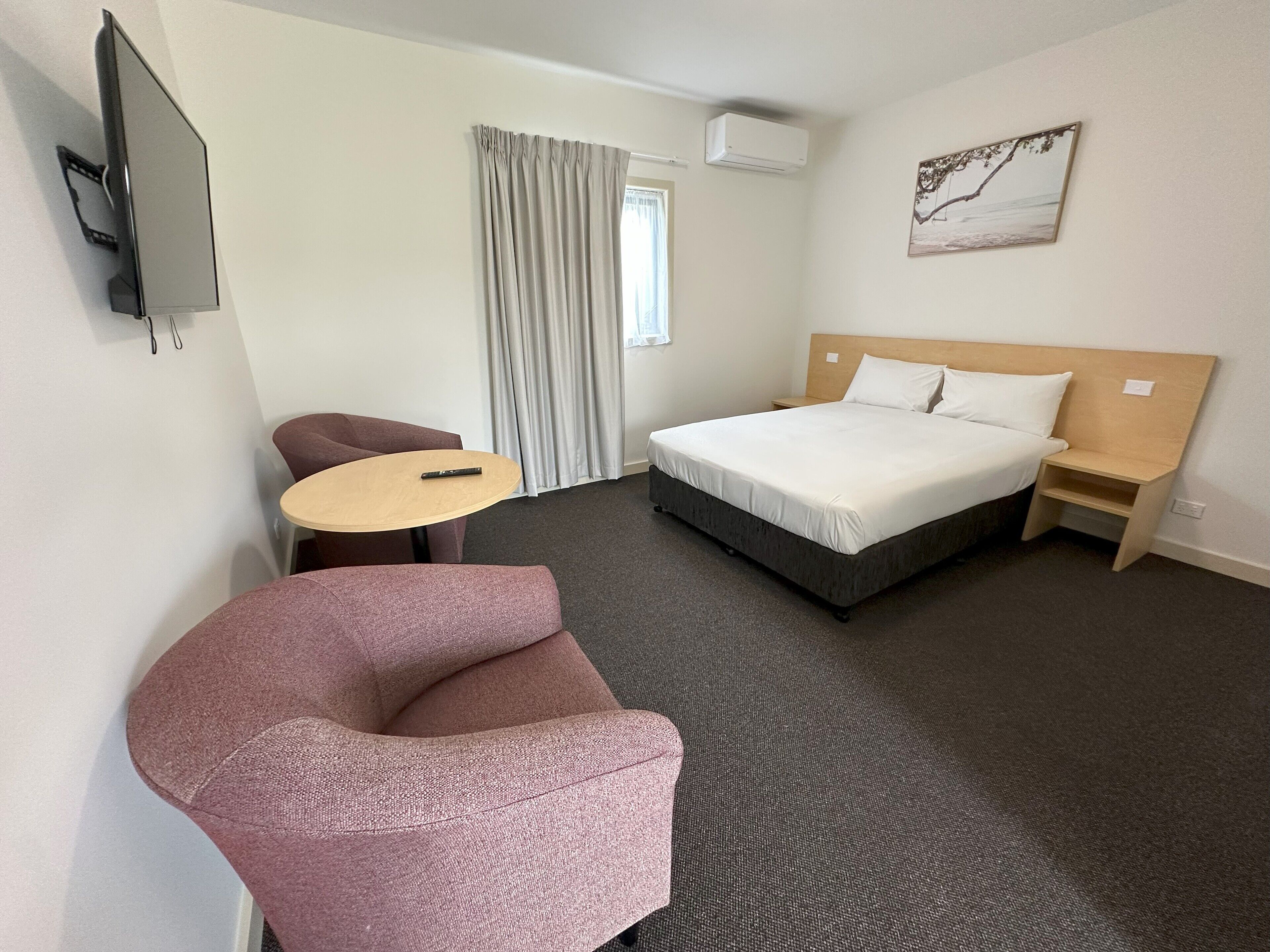 Une chambre d’hôtel avec un lit, un bureau, une chaise, une télévision et une fenêtre avec des rideaux.