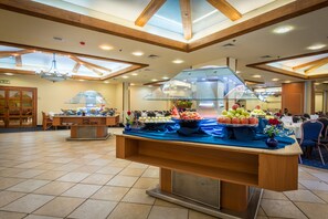 A buffet setup with a variety of food items, a glass display case, and a wooden counter. - Mary's Well Nazareth By Dan Hotels (Nazareth)