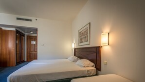 A hotel room with two single beds, a wooden headboard, a framed picture on the wall, and a door leading to another room. - Mary's Well Nazareth By Dan Hotels (Nazareth)