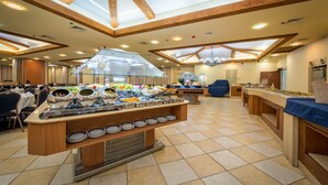 A buffet area with multiple serving stations, a central glass display, and a tiled floor. - Mary's Well Nazareth By Dan Hotels (Nazareth)