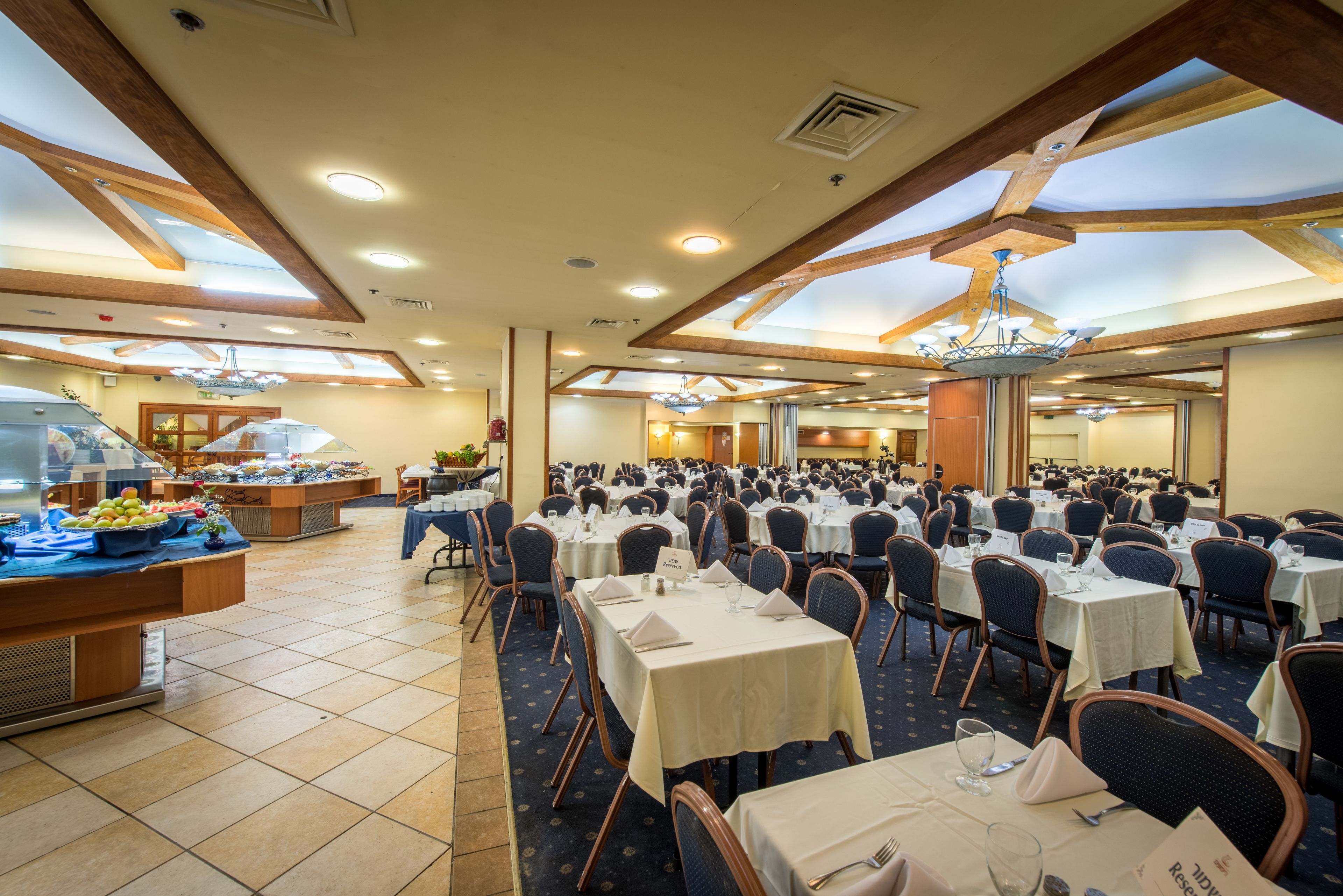 A large banquet hall with multiple round tables, a buffet area, and a high ceiling with skylights.