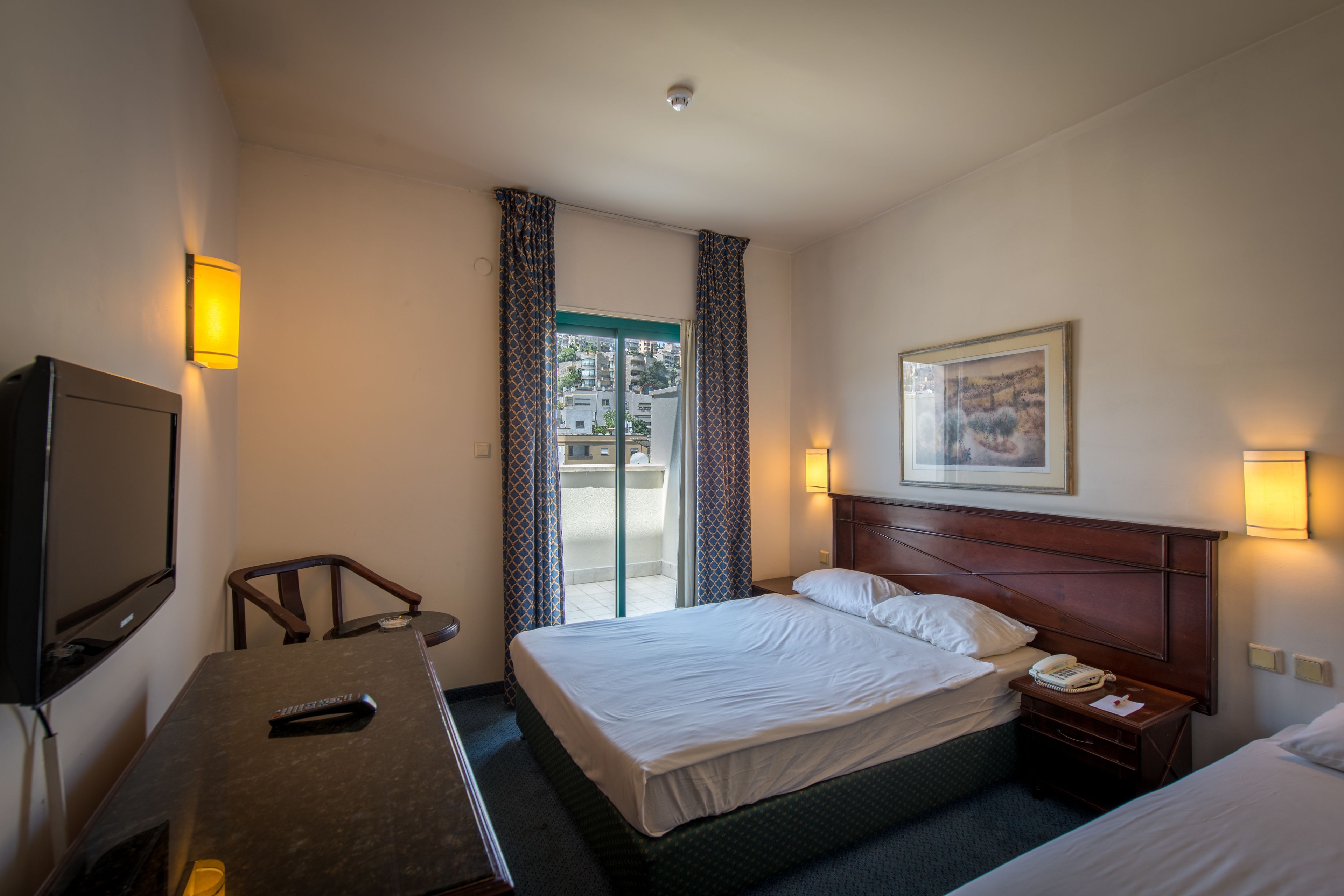 A hotel room with a bed, a desk, a chair, a television, and a painting on the wall.