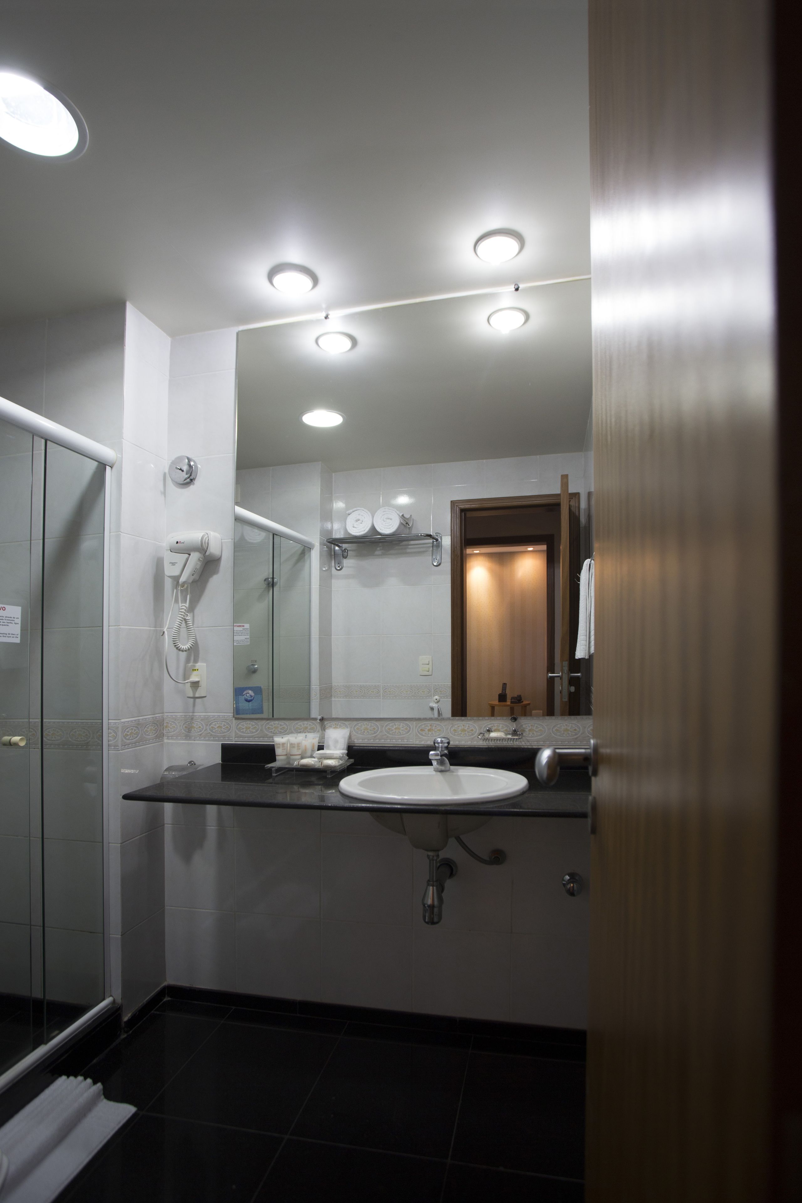 Casa de banho moderna com um espelho grande, lavatório e secador de cabelo na parede.
