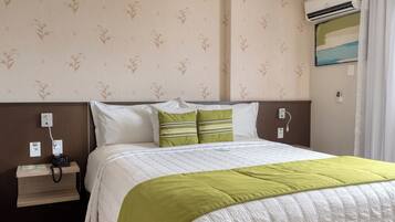 Habitación de hotel con cama, mesita de noche con teléfono, enchufe y aire acondicionado.