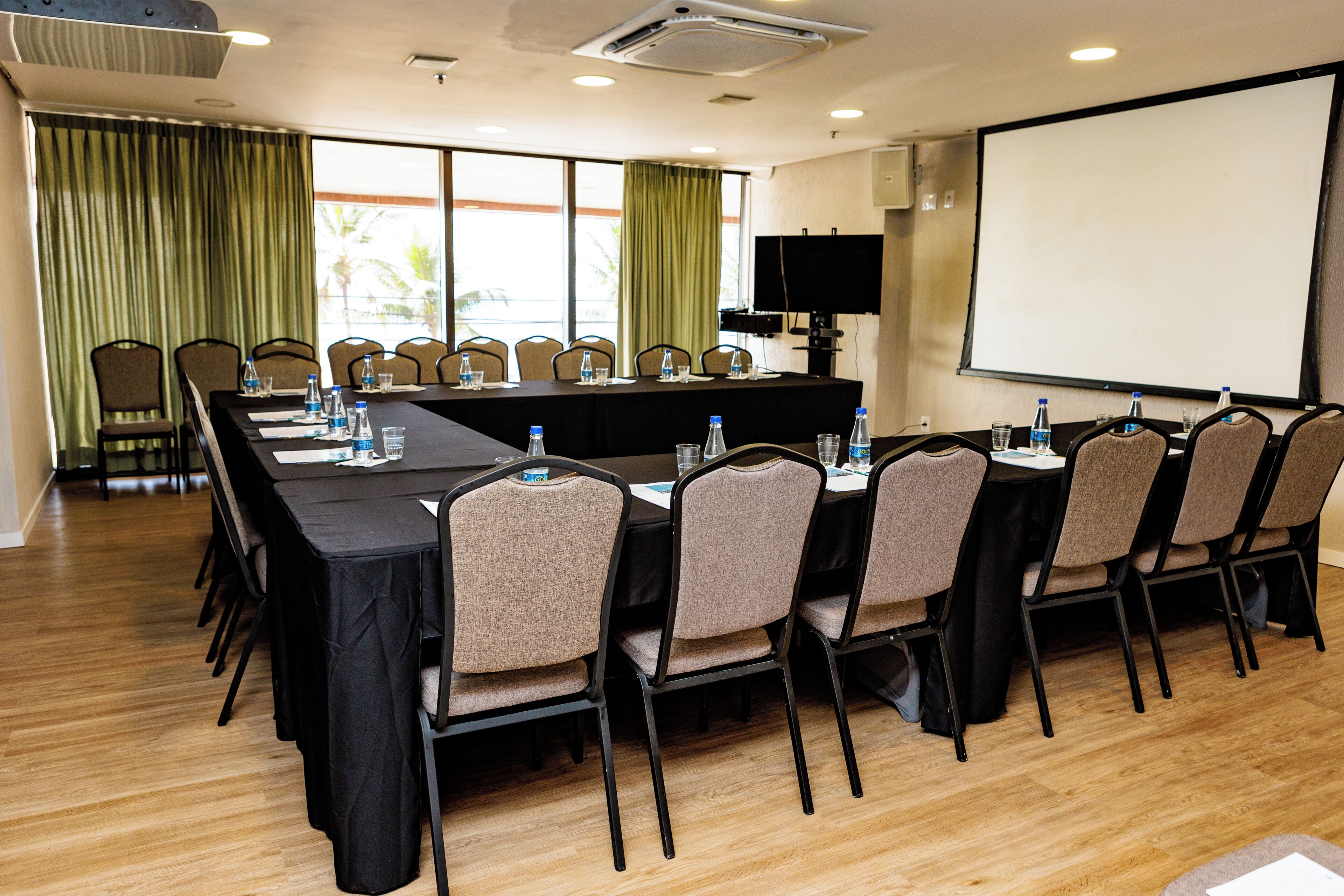 A conference room with a long table, chairs, a projector screen, and a television.