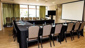 A conference room with a long table, chairs, a projector screen, and a television.