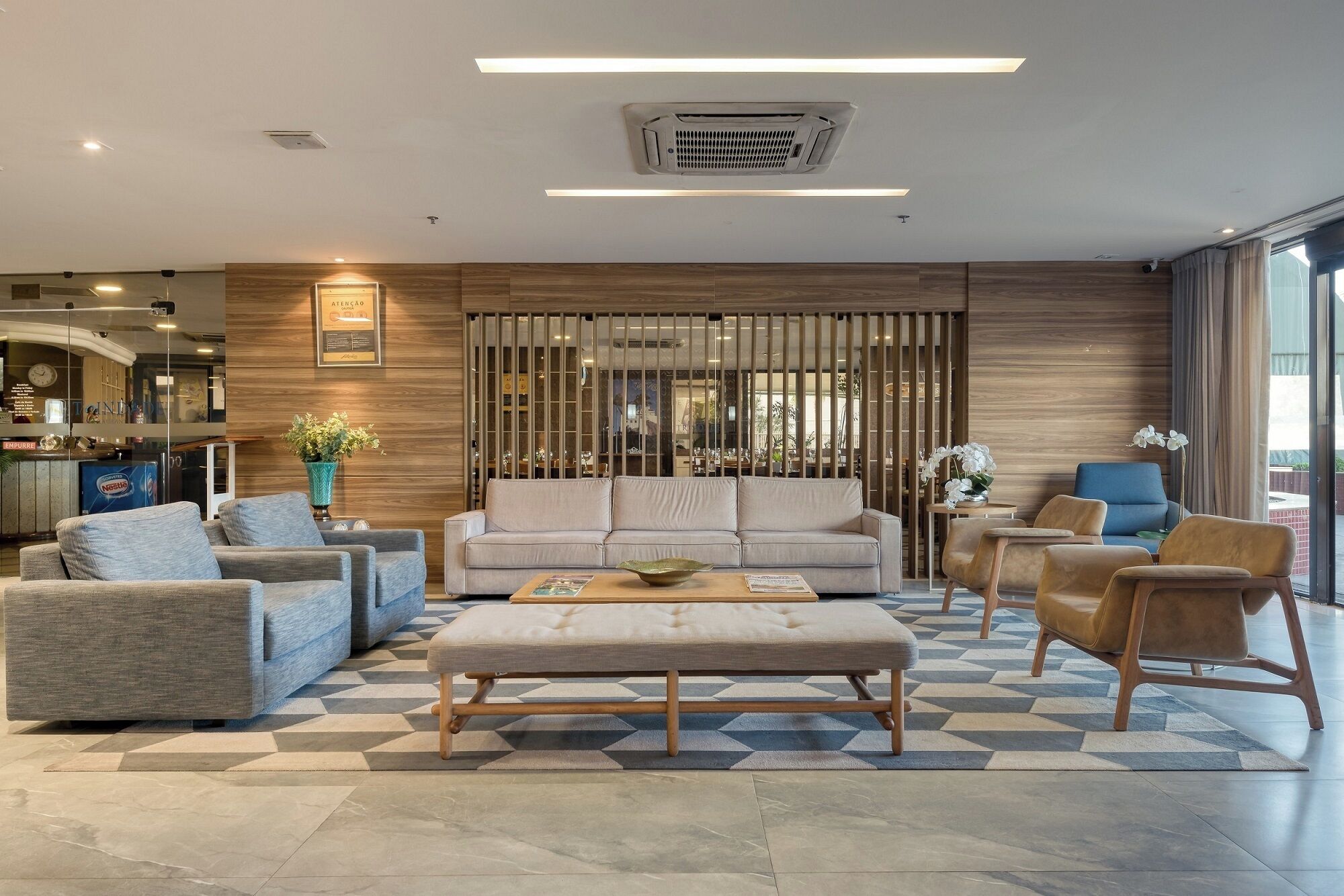A modern hotel lobby with a sofa, chairs, a coffee table, and a reception desk.