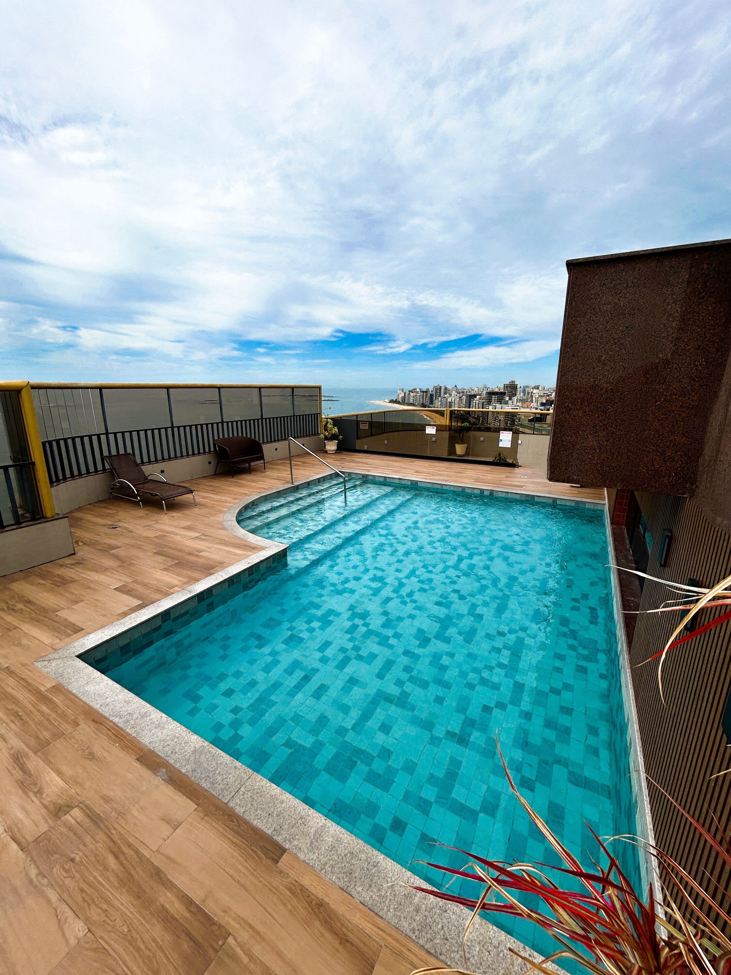 Piscina en la azotea con vistas a la ciudad, terraza de madera y sillones de descanso.