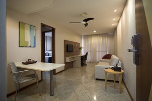 Una habitación de hotel moderna con zona de comedor, sofá, televisión montada en la pared y ventilador de techo.