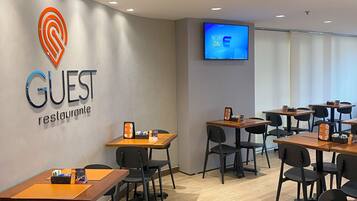 Ein modernes Restaurant mit Tischen, Stühlen und einem Logo an der Wand, sowie einem Fernsehbildschirm.