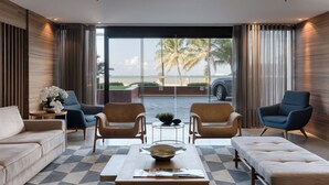 A modern hotel room with a large window, a sofa, two armchairs, a coffee table, and a view of the beach. - Quality Suites Vila Velha (Vila Velha)