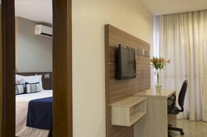 Habitación de hotel con cama, escritorio con silla, televisor de pantalla plana y un florero con flores.
