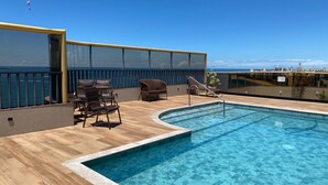 A rooftop pool with wooden flooring, wicker chairs, and a glass balustrade overlooking the sea. - Quality Suites Vila Velha (Vila Velha)