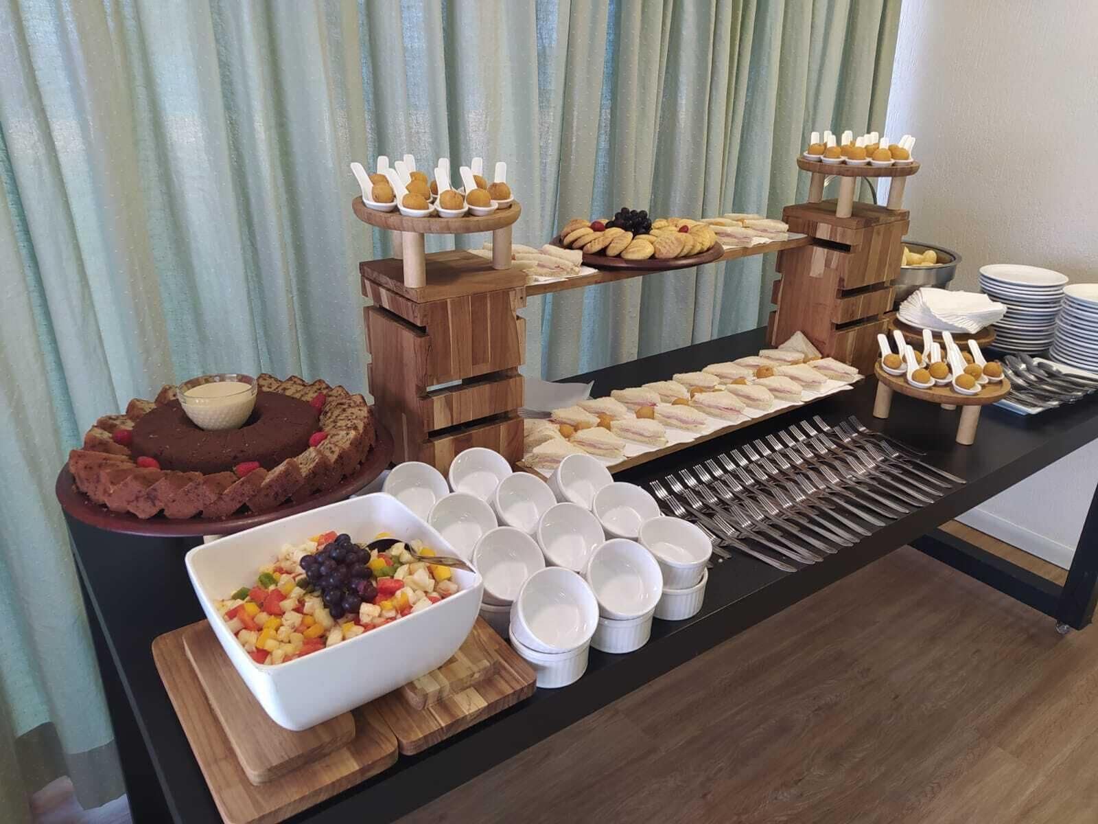 A buffet table with various food items, including a chocolate cake, fruit salad, sandwiches, and cookies.