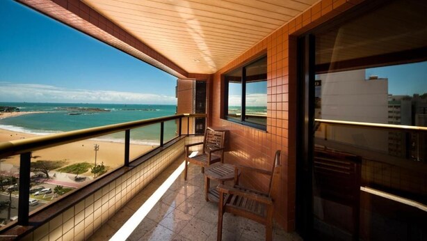 A balcony with a view of the beach, wooden chairs, and a tiled floor. - Quality Suites Vila Velha (Vila Velha)