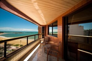 A balcony with a view of the beach, wooden chairs, and a tiled floor. - Quality Suites Vila Velha (Vila Velha)