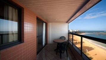A balcony with a table and chairs, a view of the beach, and a cityscape in the background.