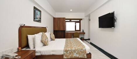 A hotel room with a bed, bedside table, a desk, a chair, a TV mounted on the wall, and a window.