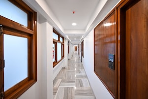 A hotel corridor with wooden doors, numbered room signs, and a marble floor.