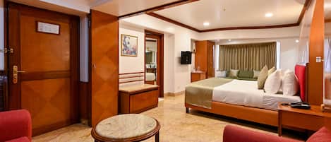 Habitación de hotel con cama, zona de estar con sofá rojo, una mesita y una puerta de madera.