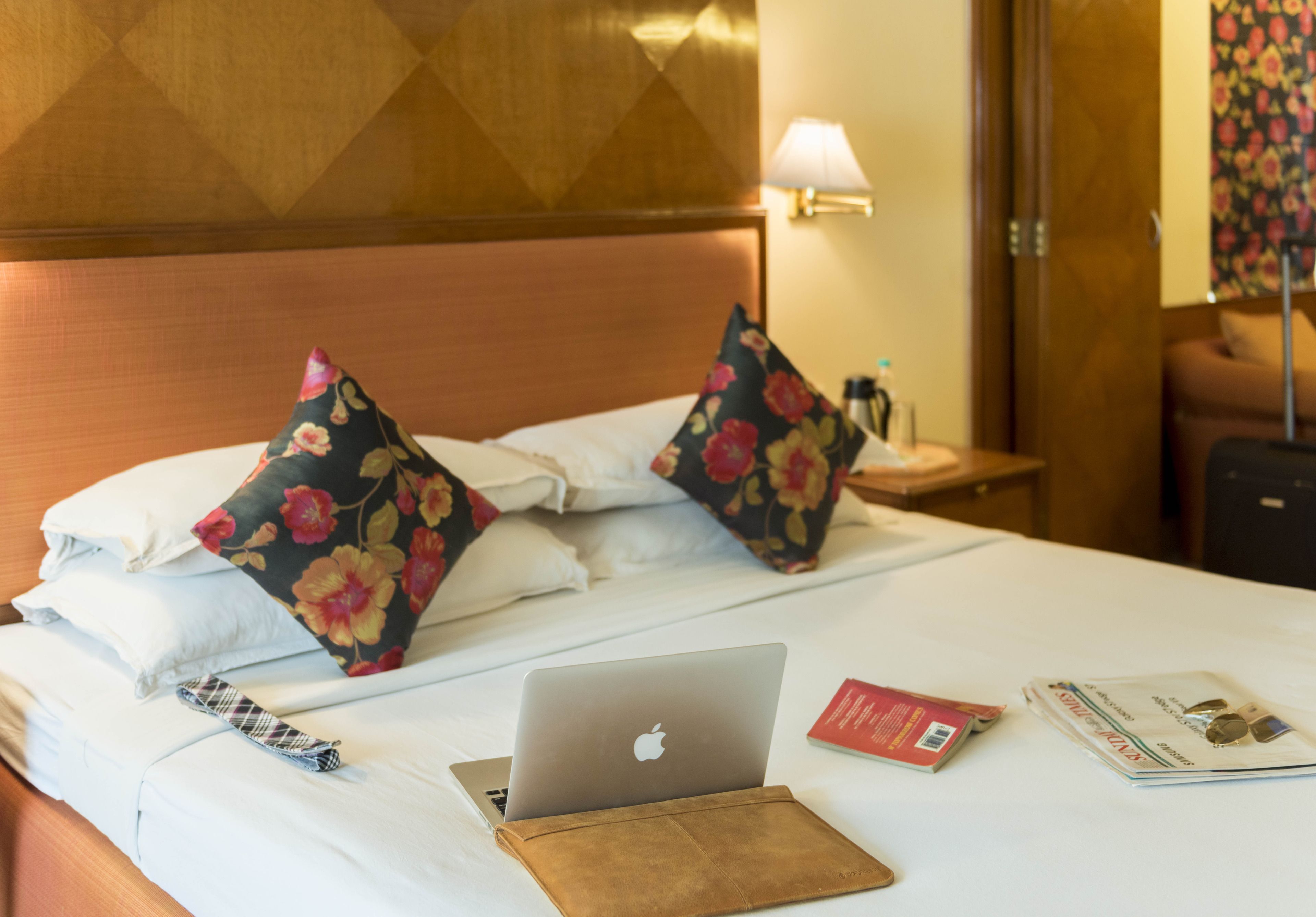 Una cama bien hecha con una laptop, una revista y una billetera encima.