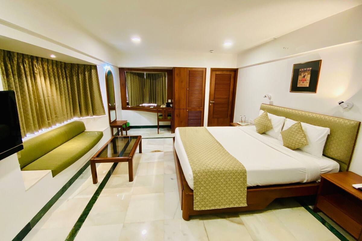 Quarto de hotel com cama, sofá, televisão, secretária e banheiro.