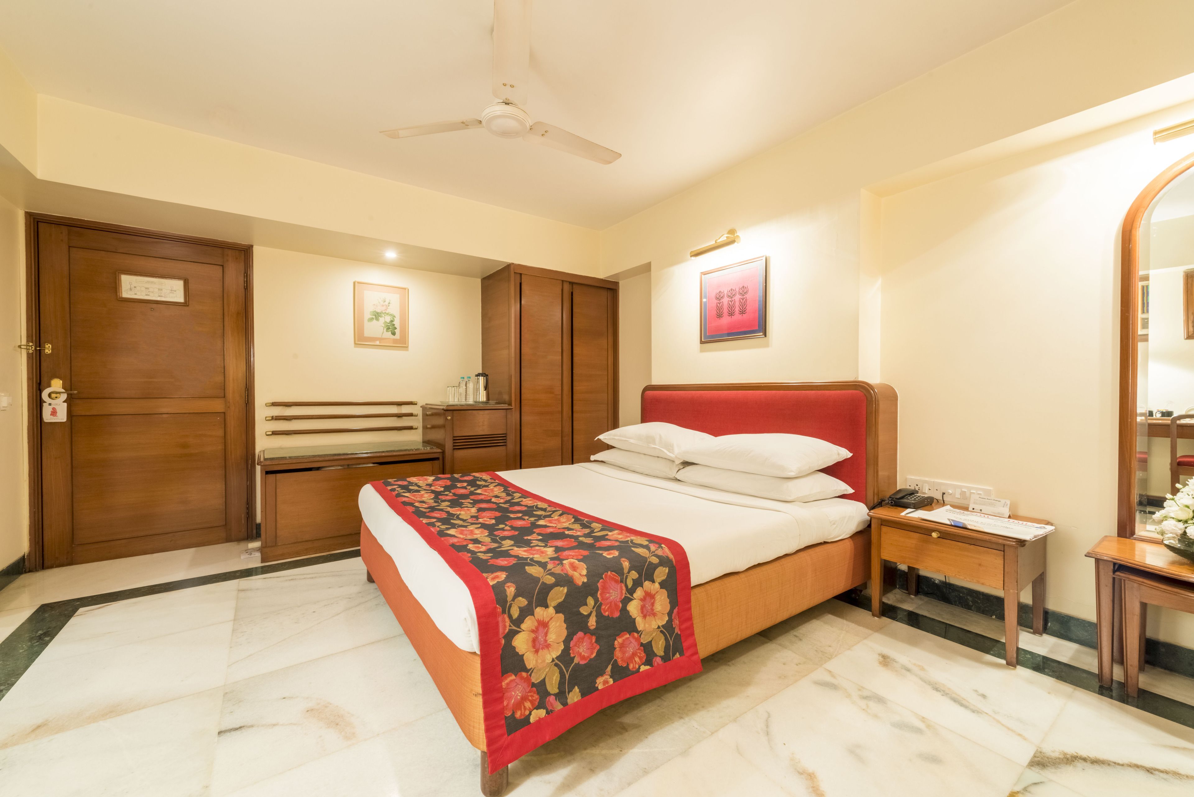 A hotel room with a bed, a nightstand, a mirror, a wardrobe, and a ceiling fan.