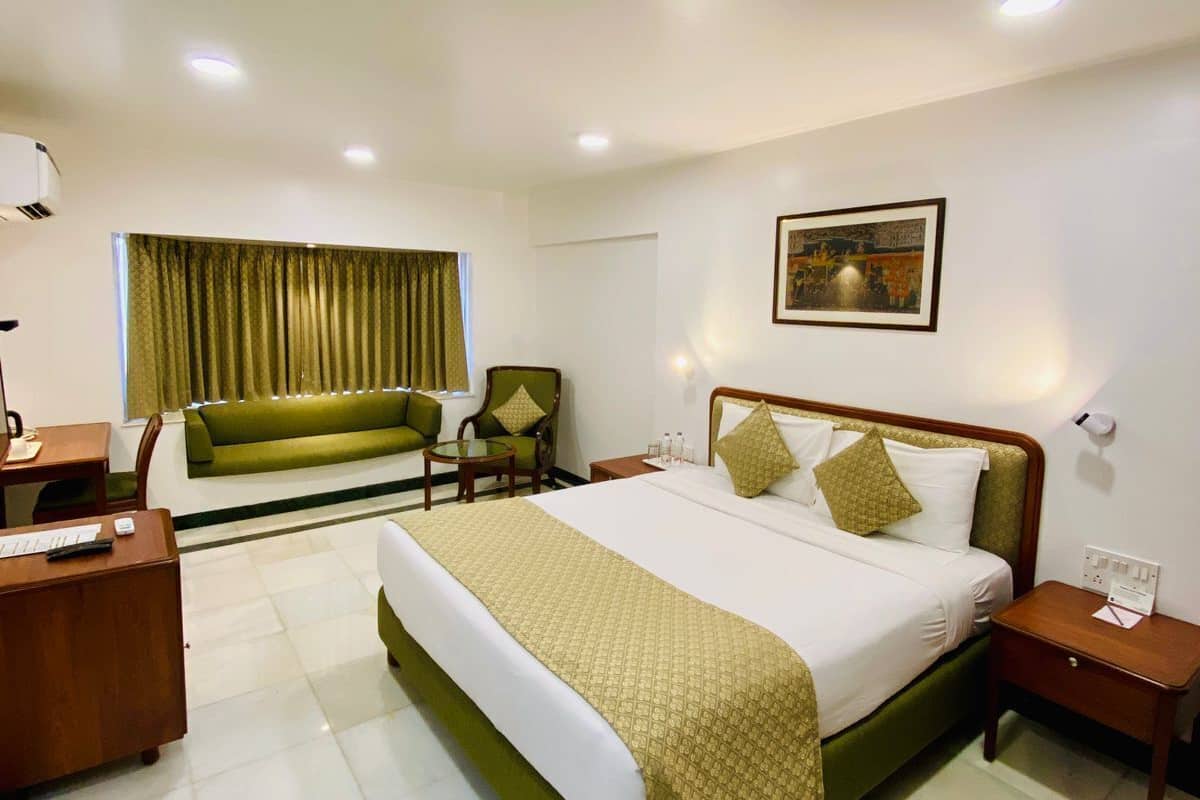Quarto de hotel com uma cama grande, uma escrivaninha, uma cadeira, um sofá e um quadro na parede.