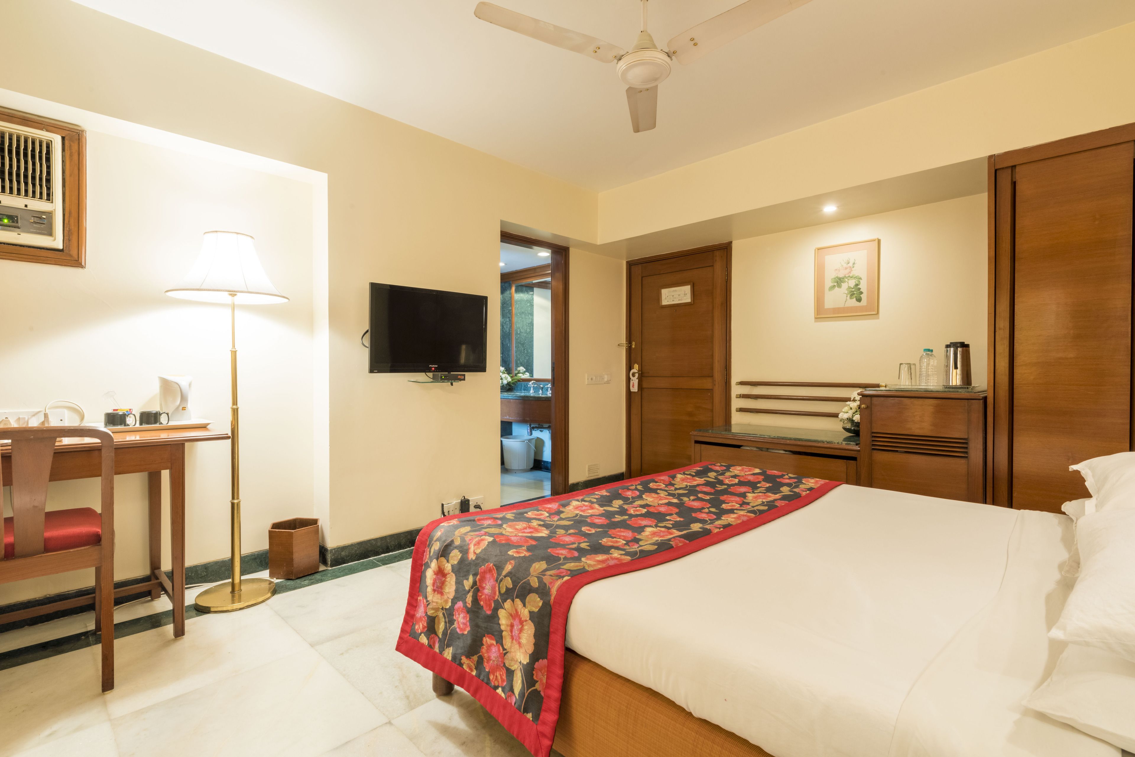 A hotel room with a bed, desk, chair, television, and a door leading to a bathroom.
